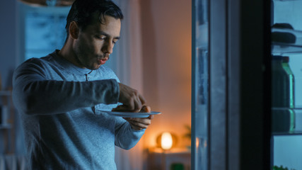 At Night in the Kitchen Handsome Attractive Young Man is Eating a Leftover Pizza from the Fridge. He is Hungry and Feels Satisfied.
