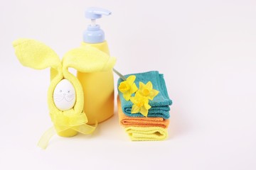 Spa and bath concept. Beautiful easter spa composition in yellow color on white background. Boatle, flower, multicolored towels, bunny from egg and yellow napkin isoleted. Copy space for text.