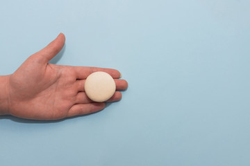 Macaroon cookie on female palm on blue flat background