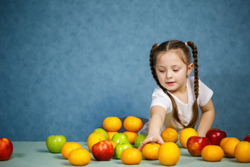 Fototapeta premium Little girl in white T-shirt plays and poses with fruit