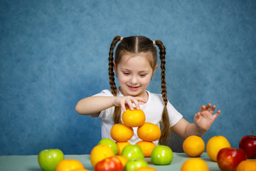 Fototapeta na wymiar Little girl in white T-shirt plays and poses with fruit