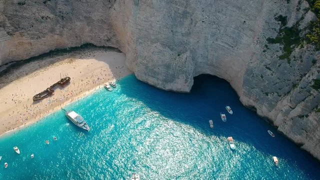 Tourists exploring the shipwreck lying on white sands of Navagio beach, surrounded by huge cliffs, Zakynthos, Greece. Aerial.