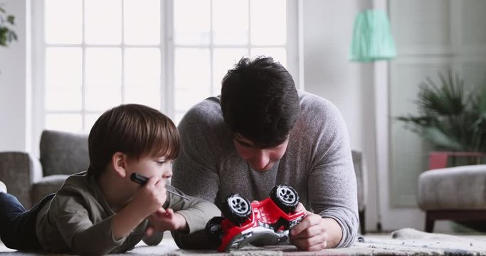 Young dad teaching preschool son play toy car at home