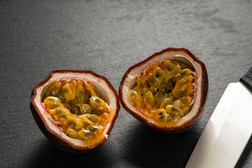 cut in half fruit passion fruit on a black campa lies next to a ceramic knife