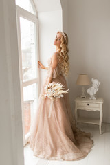 Young bride in a beautiful dress and wreath on her head holding a bouquet of flowers in bright white studio. Wedding concept.