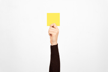 Hand of a business woman holding a yellow card in the air. Fault concept.