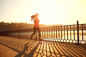 Girl runner runs in a park by the lake at dawn