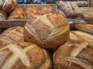 Close-up of freshly baked round loaves of bread stacked in a market display at a bakery with other types of gourmet bread in the background.