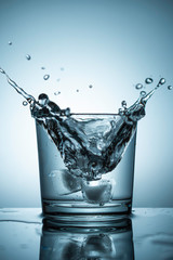 Ice cubes fall into a glass of water and fly spray