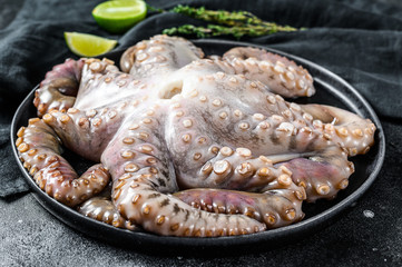 Raw octopus in a plate with cooking ingredients. Black background. Top view
