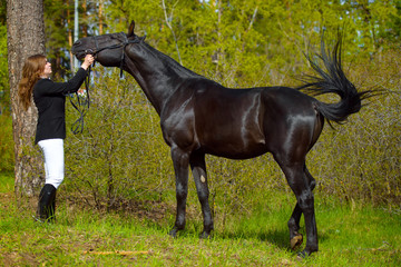 Young girl rider with a black horse in the spring