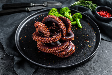 Boiled octopus with broccoli on a plate. Black background. Top view.