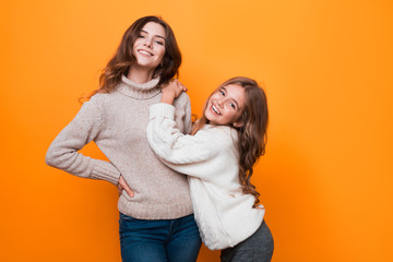 two sisters hugging and having fun in studio on orange background. age difference.