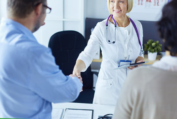 Woman doctor handshaking with a senior couple