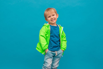 Happy blond boy child in a light green windbreaker raincoat laughing on a blue sea wave background. © evakerrigan