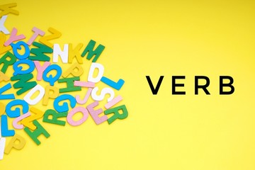 VERB text with ABC wooden letters alphabet scattered on a yellow background. Education and copy space