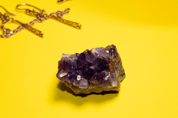 On a yellow background lies a semi-precious stone amethyst. Earrings and a bracelet are visible in...