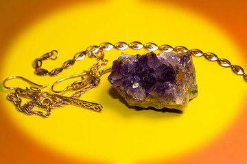 On a yellow background in an oval frame lies a semi-precious stone amethyst. Nearby are gold...