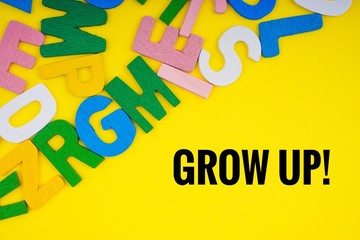 GROW UP text with ABC wooden letters alphabet scattered on a yellow background. Education and copy space