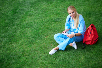 Woman doctor using tablet computer while sitting on grass.Healthcare, insurance and medicine concept