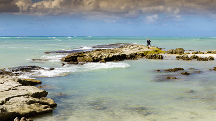 Lonely fishermen on a rocky lava-formed Hawaiian beach called Eisenhower Aqua waters, monotone and color images with bold skies.