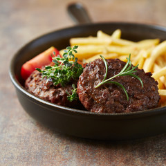 Fried hamburger steaks with tomatoes and french fries. Rustic background.