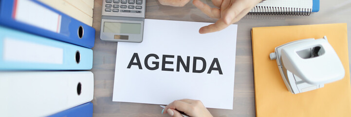 Top view of two business people hands on office table with sign agenda paper. Colourful folders and calculator laying on desk. Calendar planning and job concept