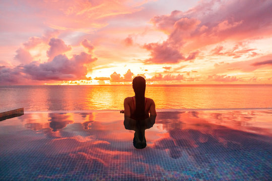 Paradise luxury resort honeymoon getaway destination at idyllic Caribbean tropical landscape hotel, woman silhouette swimming in infinity pool watching sunset serene. Winter getaway at dusk.