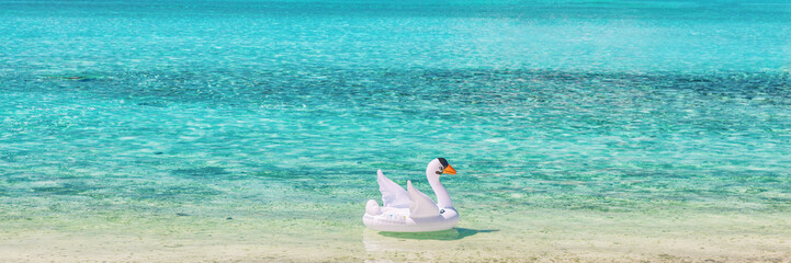Beach vacation header background travel destination in Caribbean, blue ocean water with floating swan inflatable toy panoramic. © Maridav