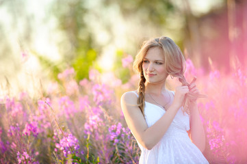 Young beautiful girl braids and walks on the spring flowered field.