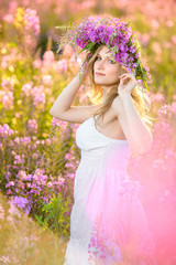 Obraz premium Young beautiful blonde girl gathers pink flowers in the spring blooming field at sunset.