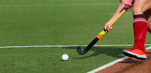 Female field hockey player passing to a team mate on a modern, water artificial astroturf field.