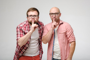 Two men say silence, making a gesture with an index finger on their lips and look excitedly at the...