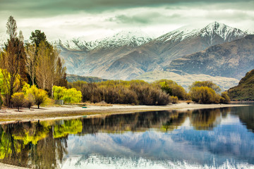 Snow capped southern alps reflected in the motionless water of the lake lined by colourful trees