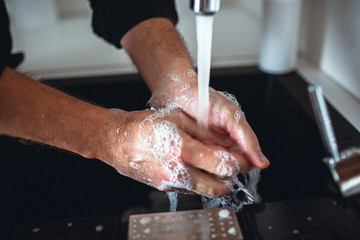 Cut view of strong man's hands washing them from soap foam under water that poures into sink from...