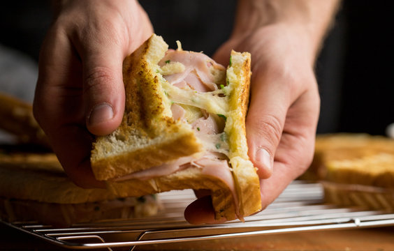 Hands tearing out French toast with cheese, ham and parsley visible stretching cheese delicious snack