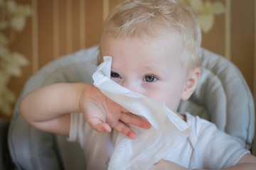 The child wipes his nose with a white handkerchief. A sick child eats sitting on feeding chair. Kid...