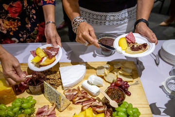 people cutting meat and cheese on wooden board