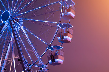 Ferris Wheel illuminated with blue lights on sunset background. Urban Scene. Copy space. Amusement...