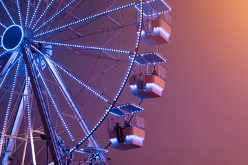 Deurstickers Ferris Wheel illuminated with blue lights on sunset background. Urban Scene. Copy space. Amusement attraction park template © Karyna