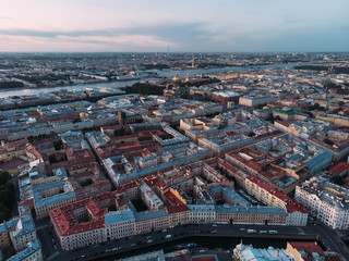 Fototapeta premium Aerial view of red and grey rooftops of Saint Petersburg. On the background St. Isaac's Cathedral and Peter and Paul Cathedral. View from above on Moyka river. Evening light. Orthodox church.