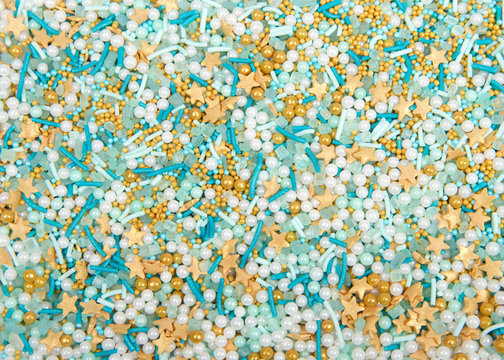 Aquatic theme background with turquoise candy sprinkles, white and turquoise balls and gold stars. Flat lay top view from above.