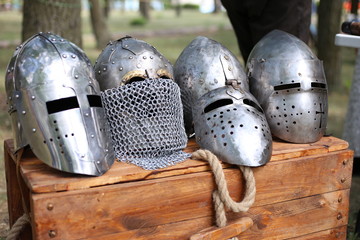Four antique metal knight helmets lie on a wooden chest