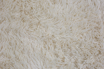 White fluffy bedspread. Shaggy texture. Beige fur blanket. Fabric background. Shaggy soft cozy carpet close-up. High pile fabric texture