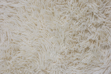 White fluffy bedspread. Shaggy texture. Beige fur blanket. Fabric background. Shaggy soft cozy carpet close-up. High pile fabric texture