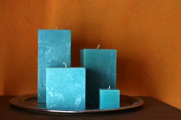 Rectangular turquoise candles stand on a metal tray near the orange wall. Moroccan style and decor. African interior