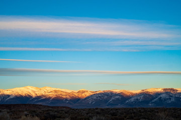 streak of dawn clouds in blue sky above snowy mouintains