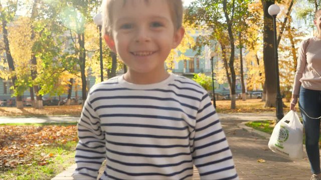 4k video of happy smiling toddler boy holding yellow mapple tree leaf running in park and looking in camera