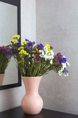 A multi-colored bouquet of dried flowers stand in a pink vase. A bouquet of flowers is reflected in the mirror. Flowers in a pink vase