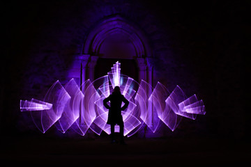Lightpainting session at night. Silhouette of a woman in front of an arch carved in stone.  Curved abstract shape made with a light saber violet. Leds light effect. Background for wallpaper.